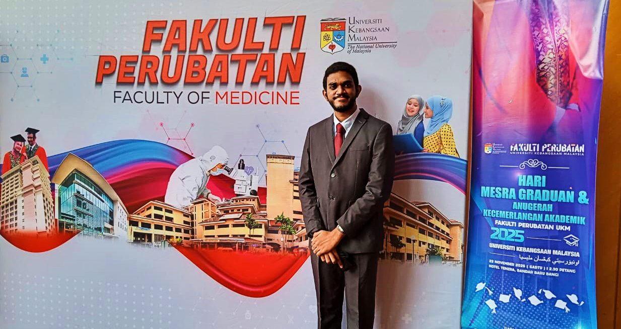 Anitej standing in front of the UKM Faculty of Medicine banner.